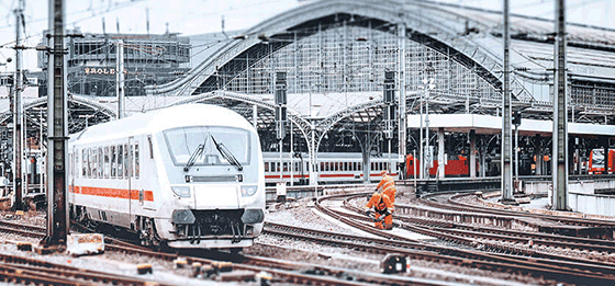 A white ICE train sets off from a main station. In the background, track workers work on the tracks